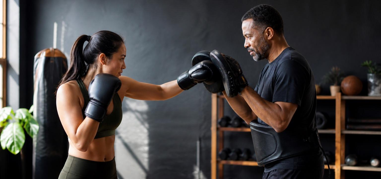 A boxing coach holding focus mitts for an athlete during training.