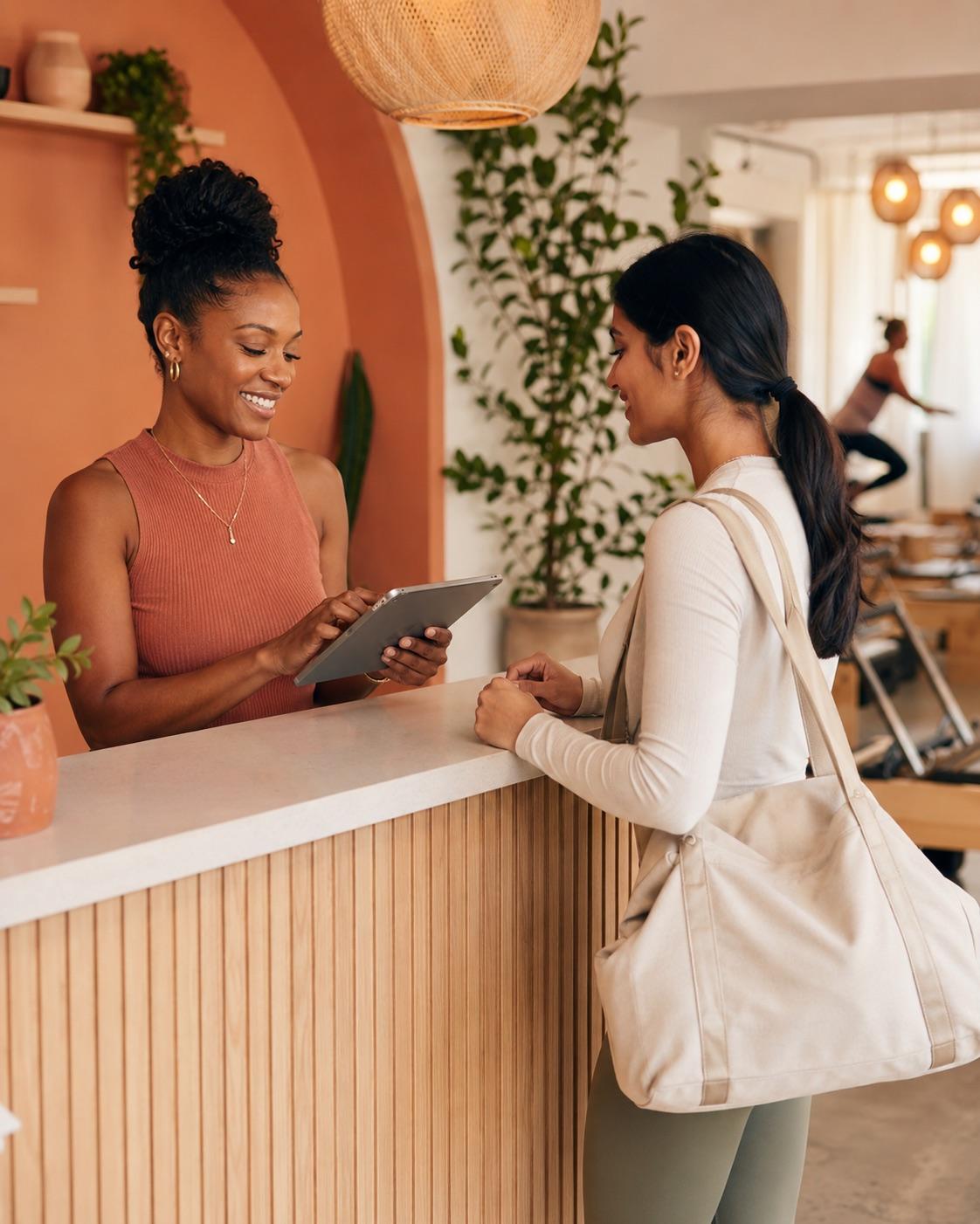 A studio owner welcoming a client at a bright Pilates studio front desk.